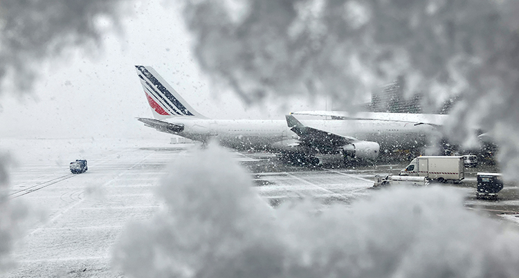 Ett flygplan står stilla vid en flygplats. Det snöar och blåser.