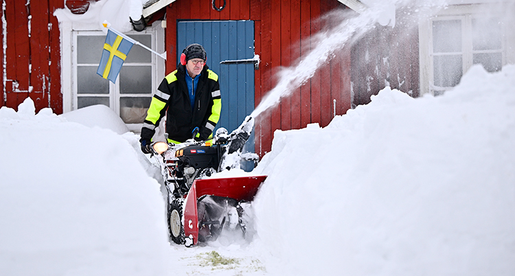 En man är utanför sitt hus och skottar snö med en snöslunga.