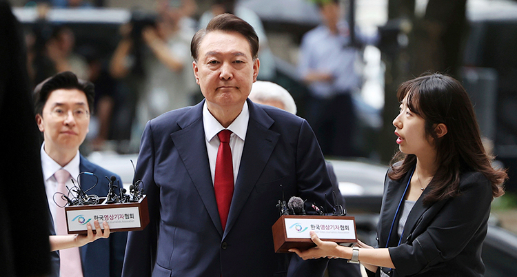 Han går mot kameran, in i ett hus. Flera journalister försöker intervjua honom.