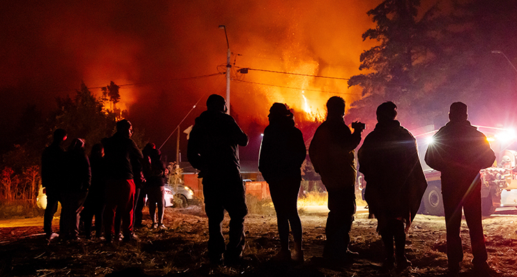 Det är kväll. Några människor är ute. En bit bort brinner det i skogen.