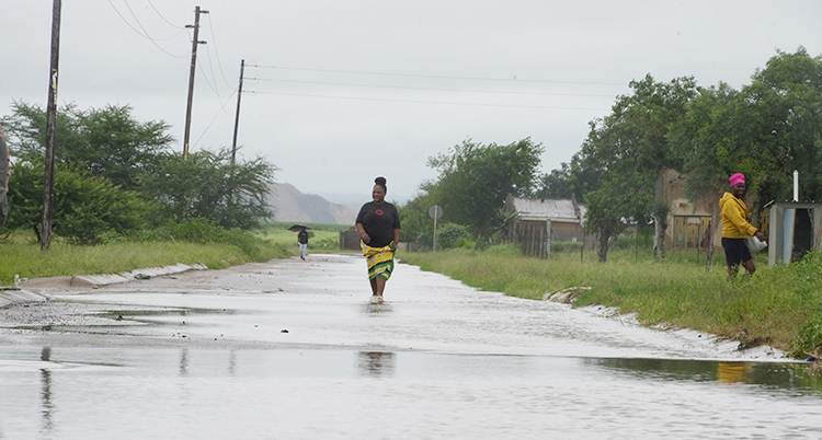 Det är massa vatten på en gata på landsbygden i Sydafrika. Några personer går på gatan.