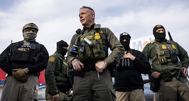 Fem poliser står bredvid varandra. Alla är maskerade utom Greg Bovino i mitten.