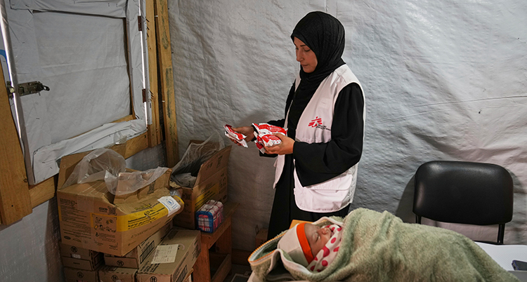 Hon står bredvid en bebis som ligger ner. De är i ett tält.