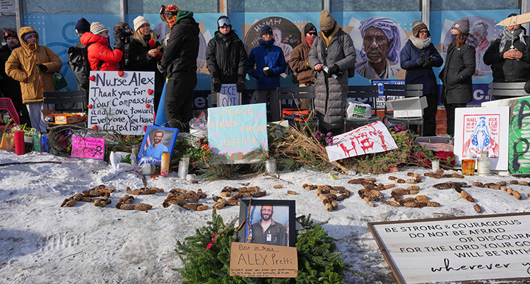Människor framför skyltar. Mannens namn är skrivet med kottar på marken.