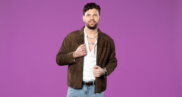 Han tittar in i kameran. Han har en skinnjacka och en tatuering på bröstet.