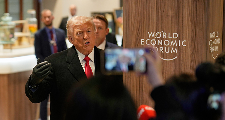 Han står i mitten. Han har slips och kostym på sig.