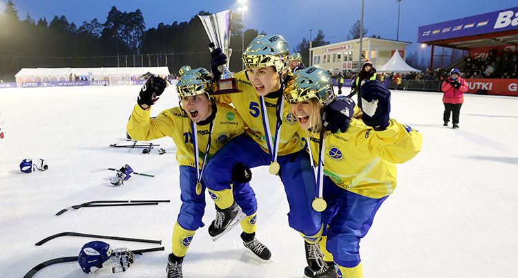 Tre kvinnor står på isen. De är glada och har guldhjälmar på sig.