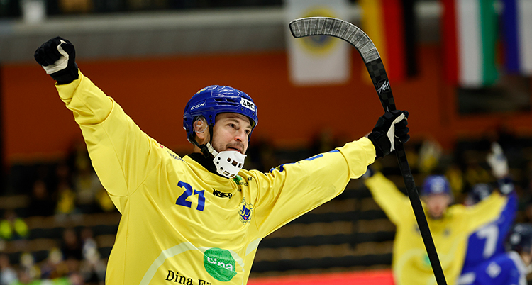 Han är glad och sträcker upp armarna i luften. Han har en bandyklubba i den ena handen.
