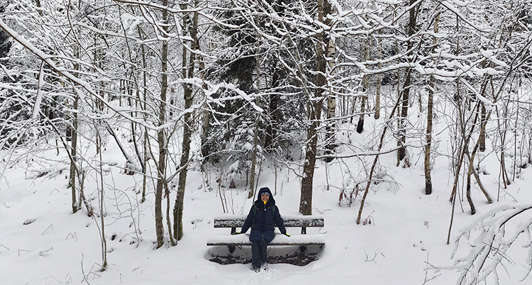 En kvinna sitter på en bänk i skogen. Det är mycket snö.