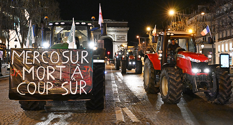 Flera traktorer kör genom Paris på kvällen. Det står saker på skyltar.