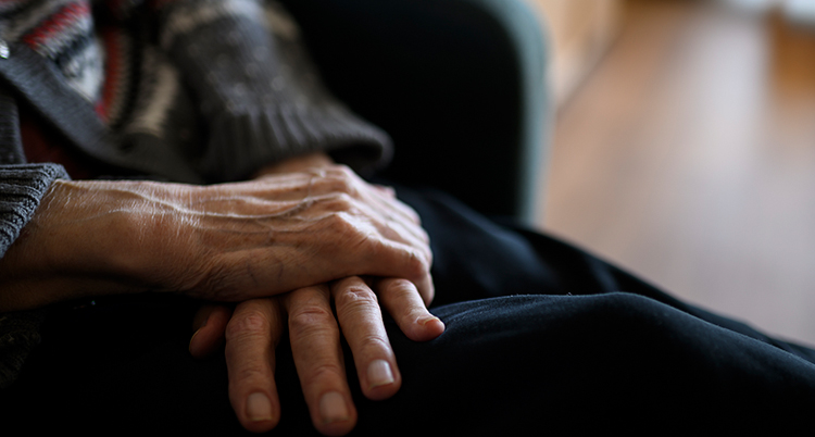 Äldre händer vilar i en persons knä.