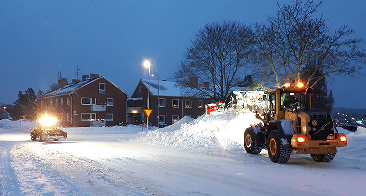 Maskiner kör bort snö. Hus syns bakom.