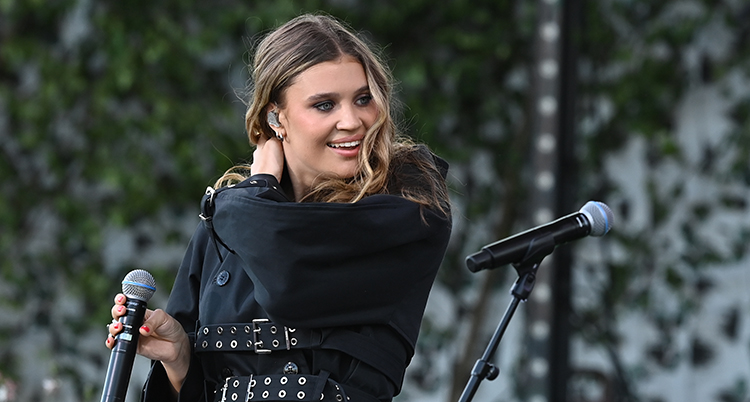 Hon håller i en mikrofon. Hon håller den andra handen på axeln.