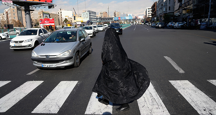 En kvinna i heltäckandes svarta kläder går över ett övergångsställe.