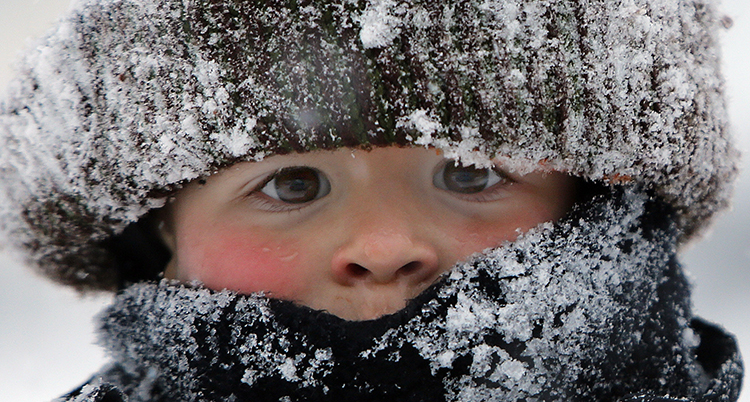 Ett barn tittar fram under en vintermössa med snö på.