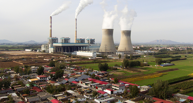 Rök stiger mot himlen från ett stort kraftverk. Intill ligger en staden med hus.