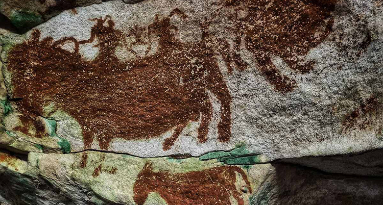 Röda bilder på djur och människor som rider på djur är målade på grottans vägggar.