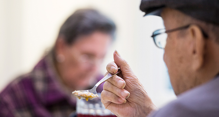 En gammal man sitter och håller i en sked. Det är mat på skeden.