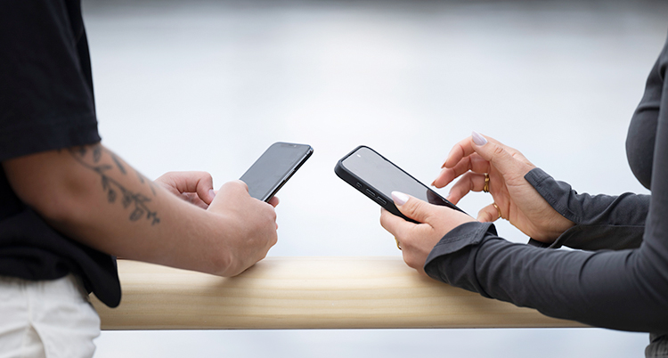 Två personer står vid ett bord. De har varsin mobiltelefon som de tittar på.
