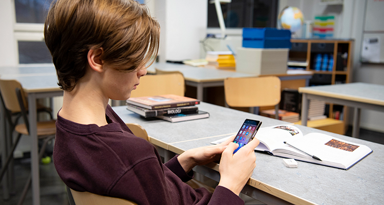 En pojke sitter i sin skolbänk och kollar på mobilen.