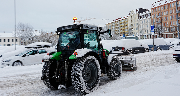 En traktor med plog på en snöig gata i en stad.