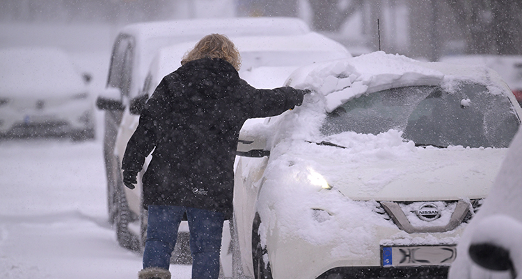 En kvinna borstar bort snö från sin parkerade bil.