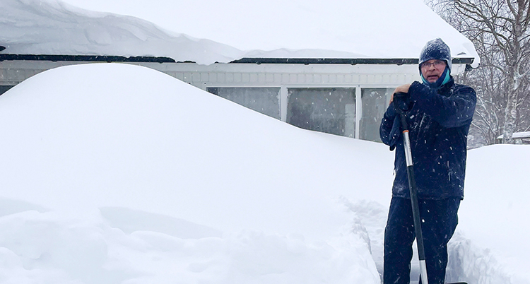 Han står i snön framför ett hus med mycket snö.