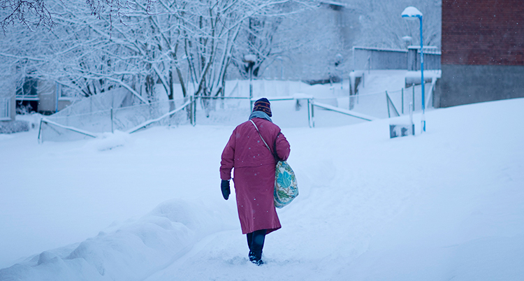 En kvinna går i snön på en gångväg. Vi ser henne bakifrån.