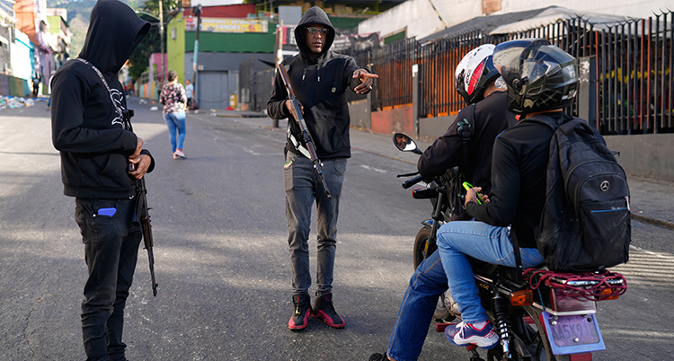 Två personer med vapen står på gatan. De stoppar en moped.
