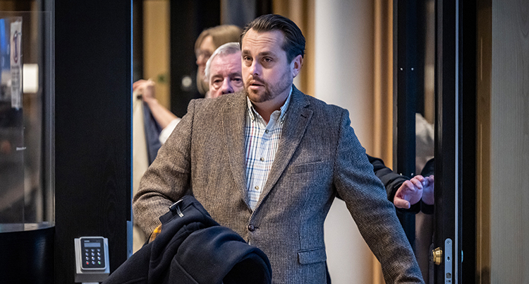 Han har öppnat en dörr och bär sin jacka på armen.