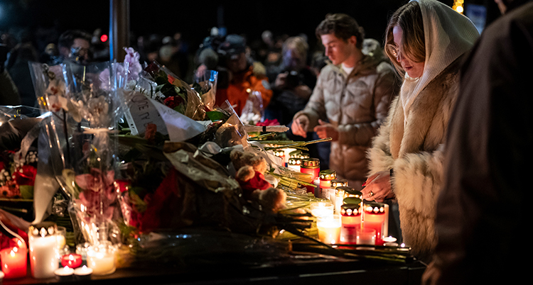 Tända ljus står på ett bord. Där ligger också blommor. Människor är samlade runt bordet.