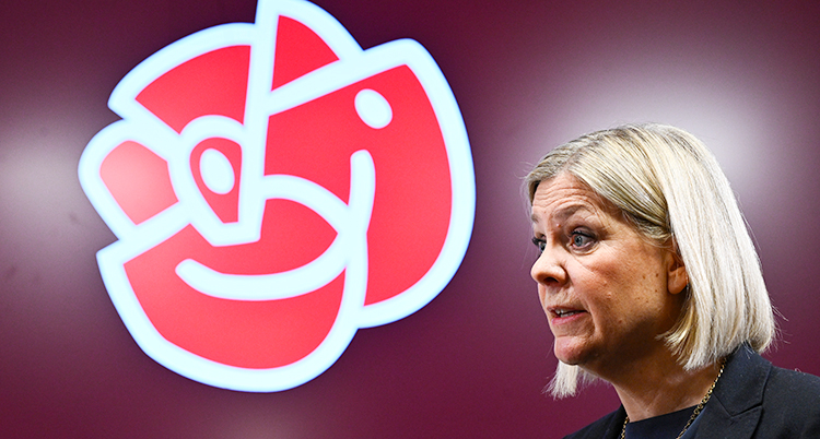 Hon står och pratar. Bredvid henne är Socialdemokraternas symbol, en röd ros.