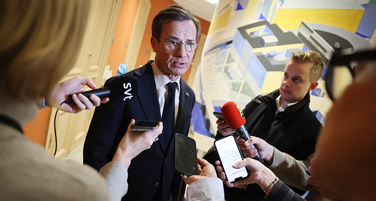 Han står och pratar. Journalister sträcker fram sina mikrofoner till honom.