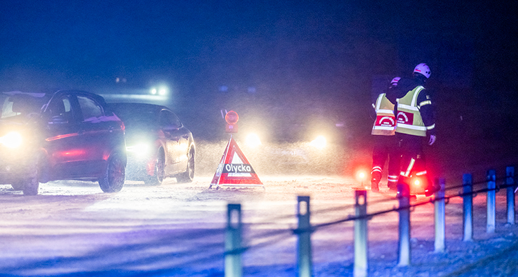 Det är mörkt och det är snö och blåst i luften. Flera lampor från bilar lyser.