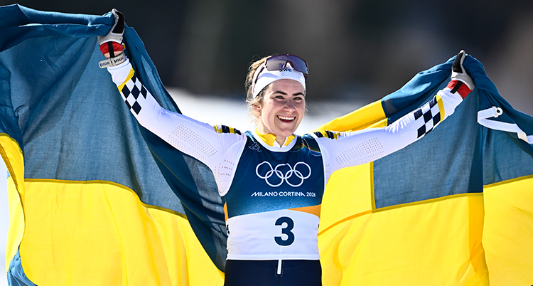 Hon håller en stor svensk flagga bakom ryggen. Hon är glad.