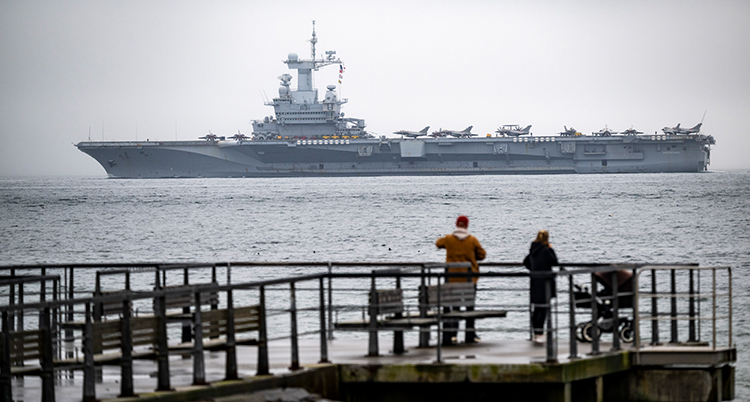 Folk tittar ut över havet. Där kör ett stort fartyg.