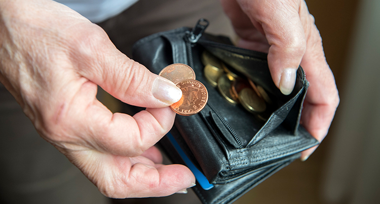 En äldre person håller upp ett par mynt från en plånbok.