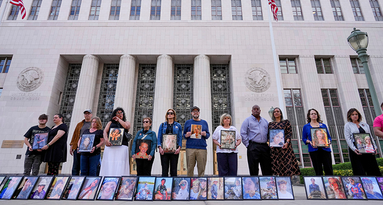 Flera personer står bredvid varandra framför ett stort hus. De håller i fotografier och på marken finns fotografier.