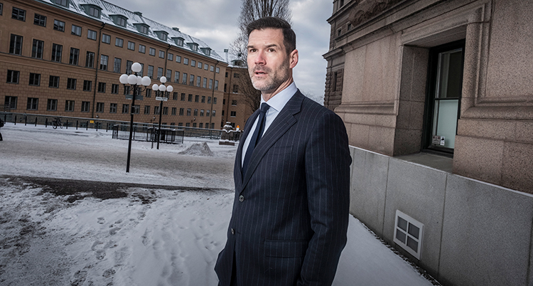 Han står utanför riksdagen i Stockholm. Han har kostym och slips. Det är snö på marken.