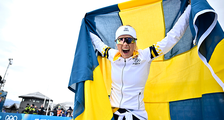 Hon håller i en flagga. Hon har solglasögon och jublar.