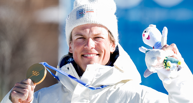 Han är glad. Han håller upp en medalj och ett gosedjur.
