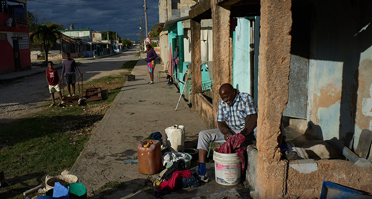 EN man sitter på en smutsig gata och tvättar kläder i flera hinkar.