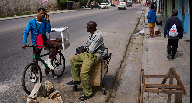 Två människor pratar vid en gata i en stad. En av dem sitter på en cykel.