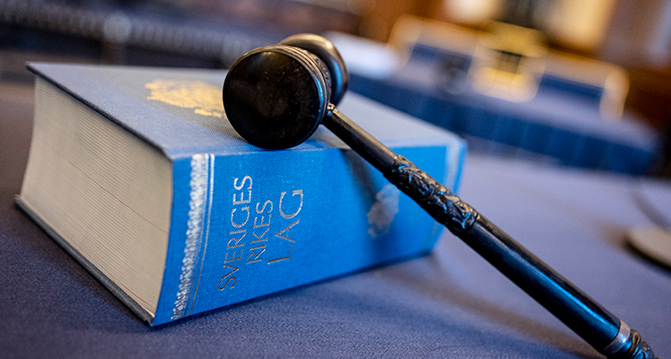 En stor blå bok med Sveriges lagar. På boken ligger en klubba av trä.