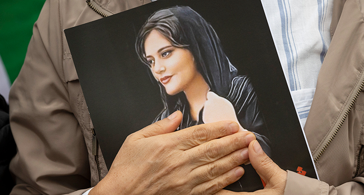 En person står och håller i en bild. Bilden visar kvinnan Mahsa Amini.