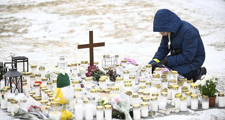 En kvinna sitter på knä vid ett hav av blommor och ljus.
