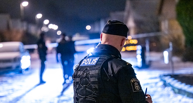 Det är mörkt. Polistejp har spärrat av en gata. En polisbil och flera syns.