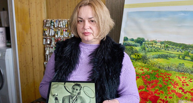 En kvinna som ser allvarlig ut. Hon håller i ett fotografi som visar en ung kvinna.