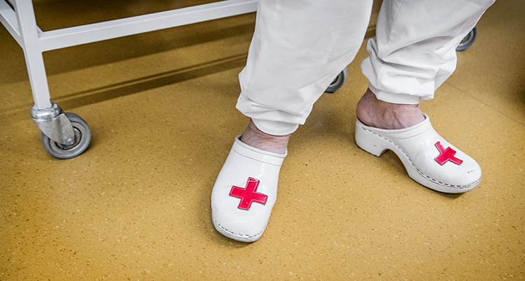 Benen på en kvinna i vita kläder och tofflor med röda kryss på.