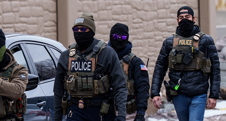 De går längs en gata. De har västar med mycket utrustning. De har också pistoler.